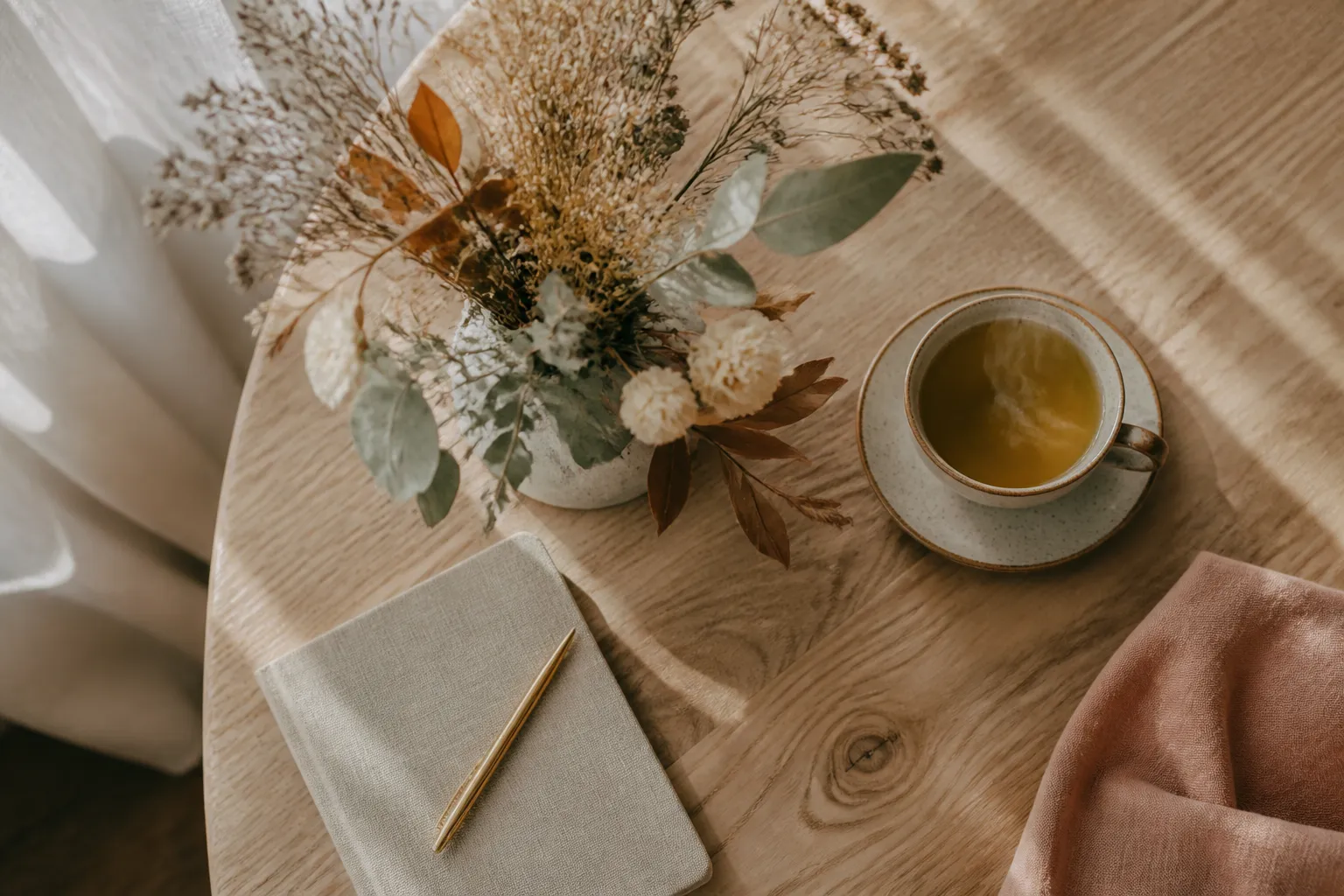 Table en bois avec plantes séchées, tasse de tisane fumante et carnet en lin